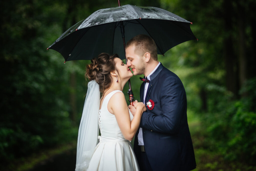 Brautpaar küsst sich unter einem Regenschirm